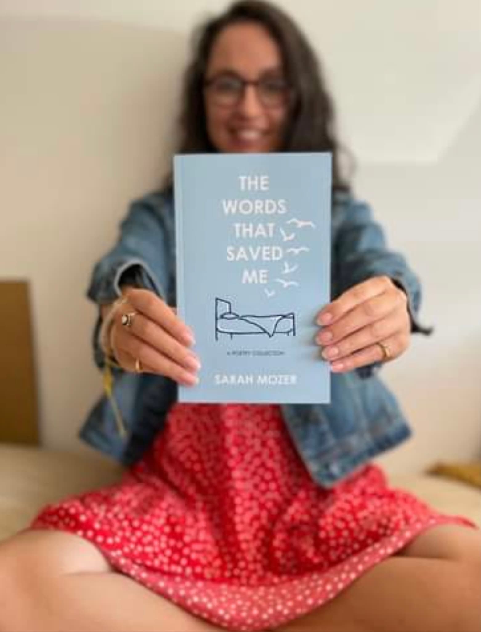 Sarah holding her book The Words That Saved Me while seated indoors