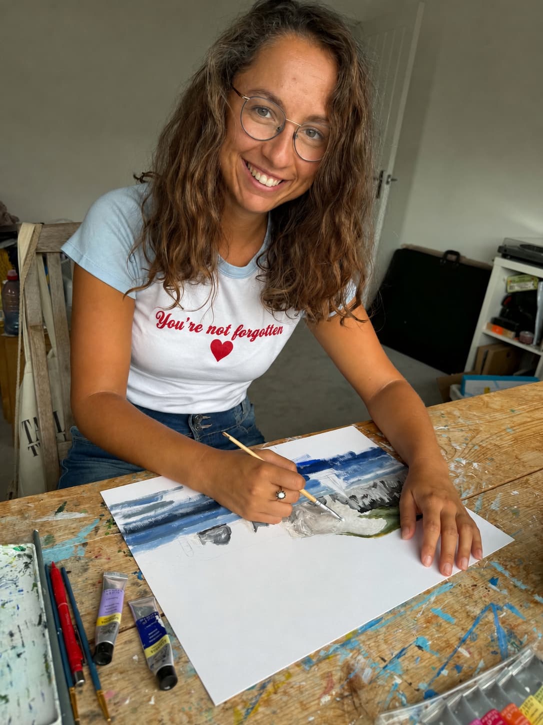Image of a 30 something white woman sitting at her desk painting